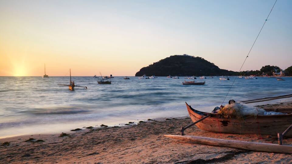 A beach with boats and a hill in the background.