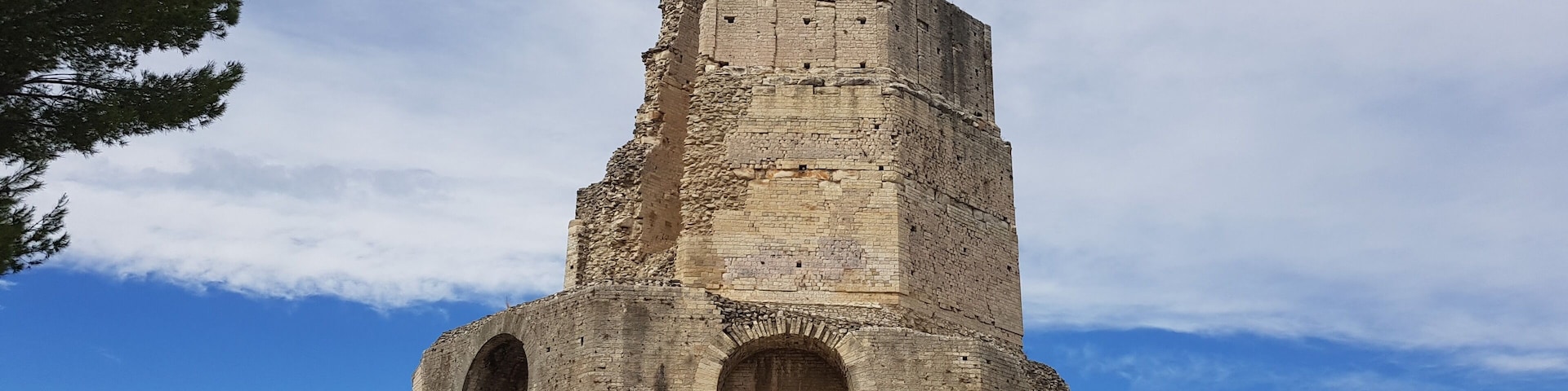 Una torre de piedra grande y antigua con puertas arqueadas, rodeada de árboles y un cielo despejado.