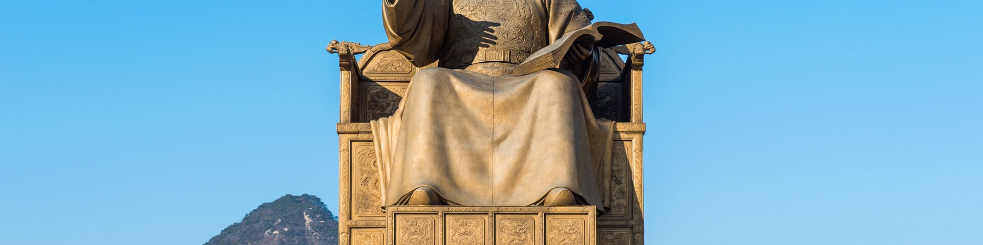 Uma estátua de uma figura sentada em um pedestal com inscrições.