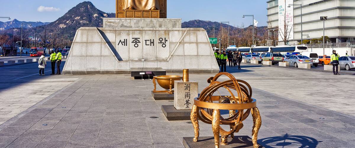 A statue of a seated figure with inscriptions, a golden astronomical instrument, and a modern building in the background.
