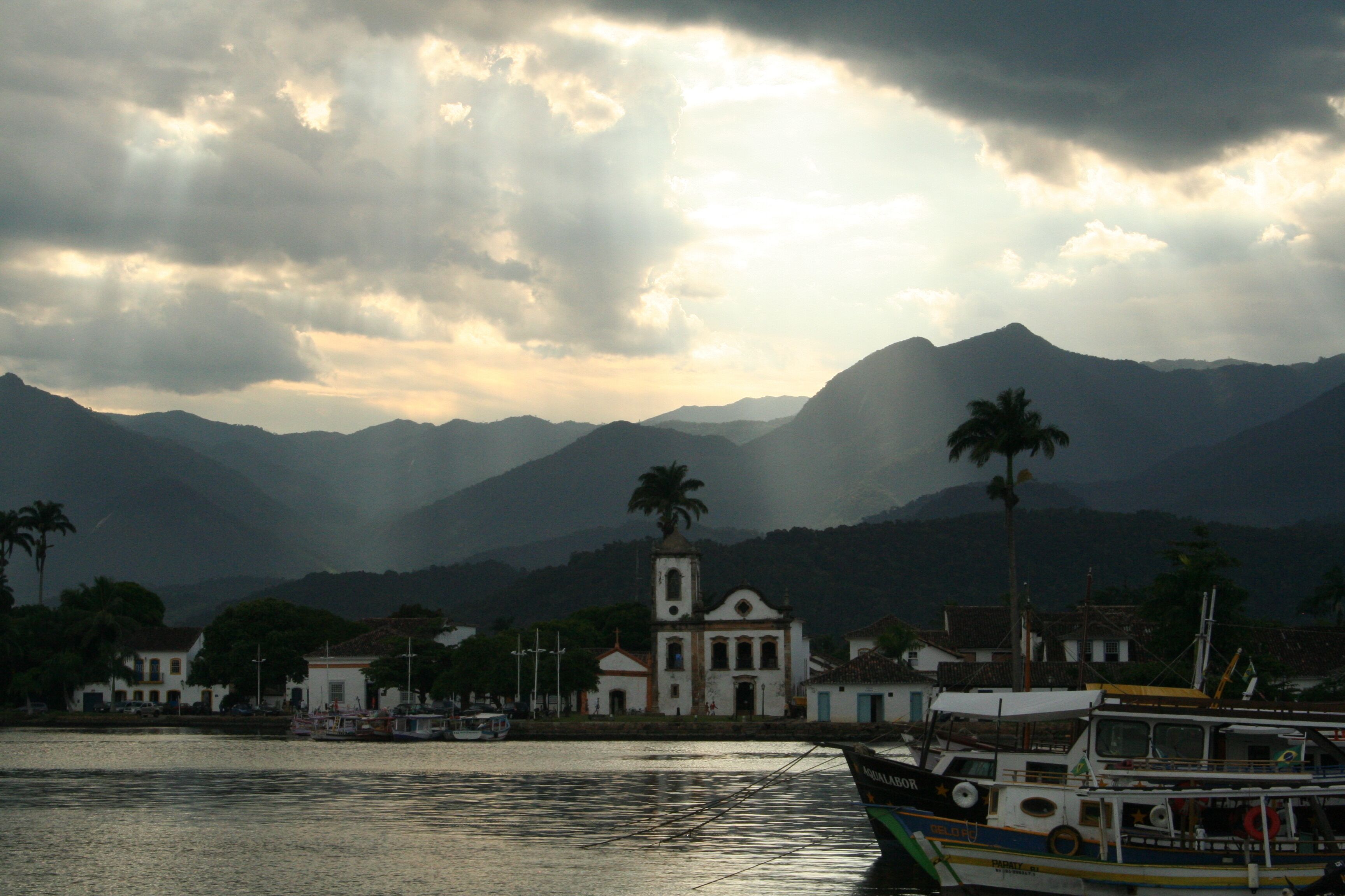 A coastal town with a church, boats, and mountains in the background.