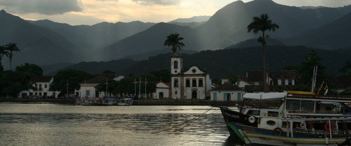 A coastal town with a church, boats, and mountains in the background.
