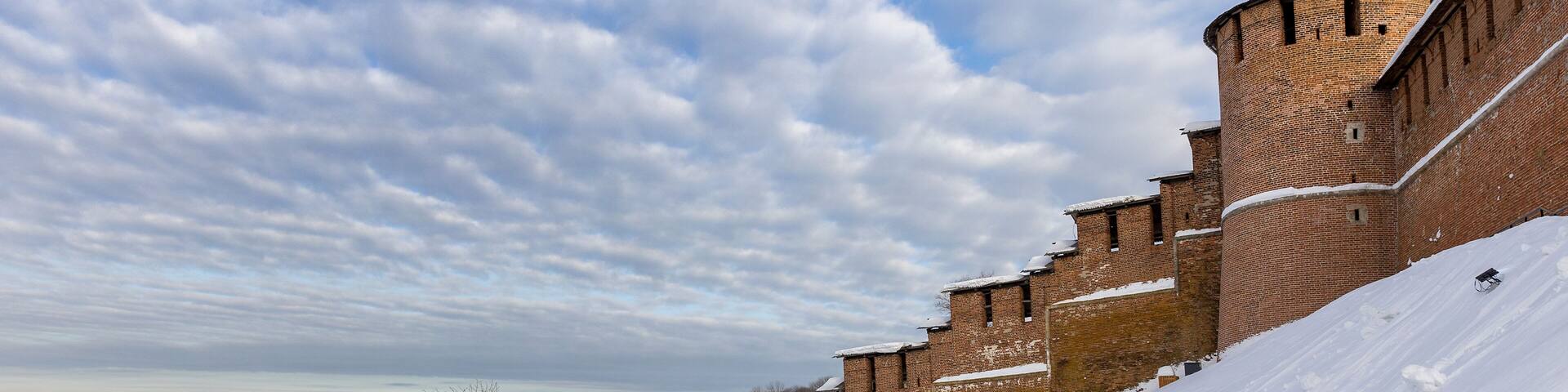 A snow-covered brick wall with a tower and a church with a green dome.