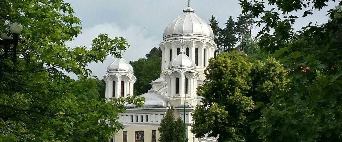 A large white church with domes, surrounded by well-maintained gardens and trees.