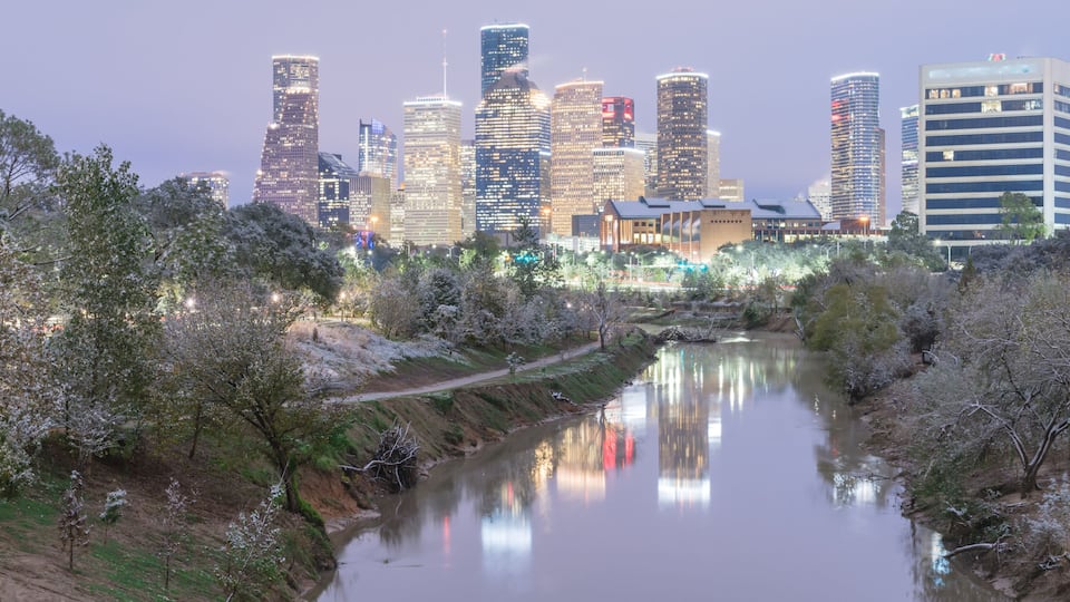 Silhueta urbana com edifícios modernos e um rio refletindo as luzes.