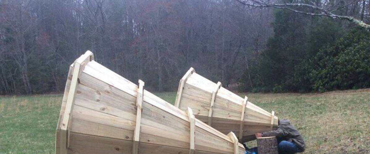 Two large wooden boats leaning against a tree stump in a grassy area with trees in the background.