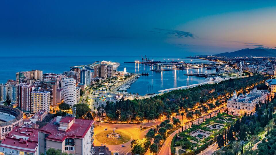 Night aerial panorama of Malaga, Spain with skyscrapers, streets, port, city hall and park during golden hour