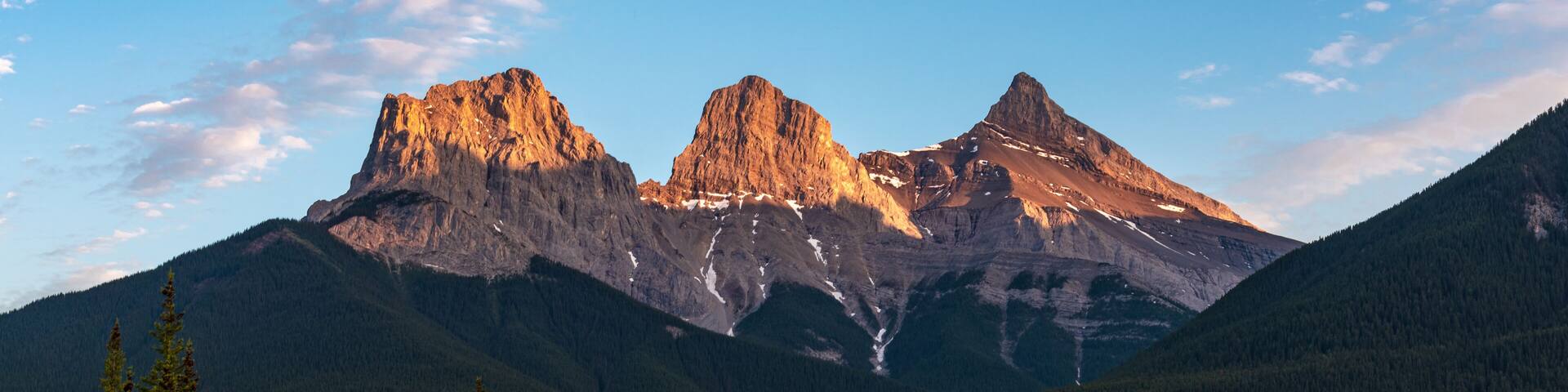 Three Sisters in Canmore seen at golden hour, sunset on blue sky day, afternoon with calm, peaceful reflection in water below famous, tourist, tourism mountains, area summer.