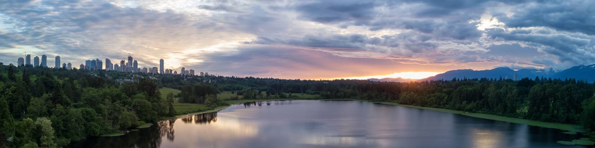 A lake with a city skyline in the background, surrounded by trees and mountains.