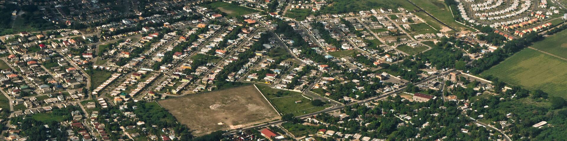 An aerial view of a densely populated residential area with a mix of single and multi-story houses, surrounded by green spaces and roads.
