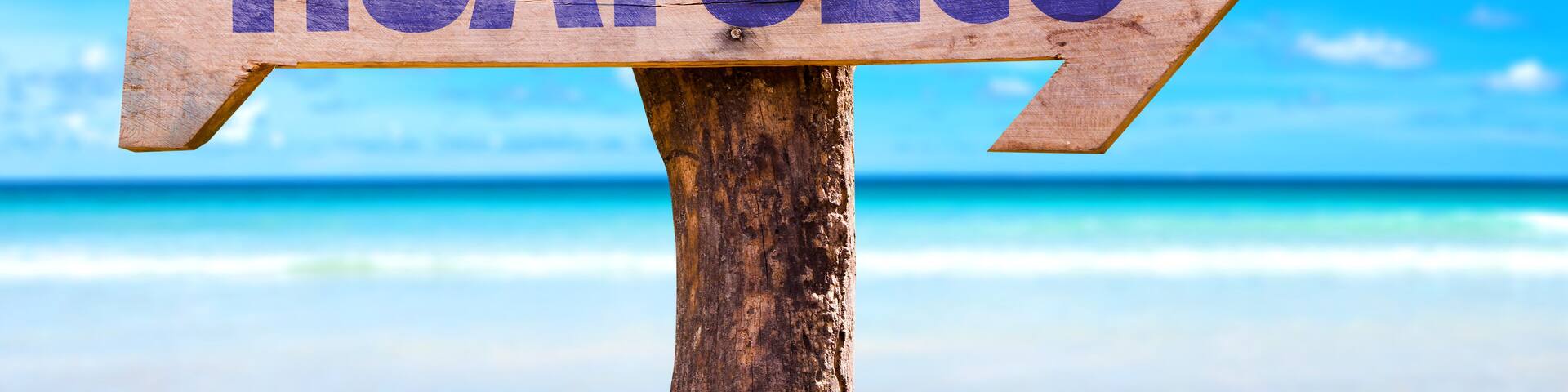 A wooden sign with the word "HUATULCO" pointing to the right, set against a beach and clear blue sky.