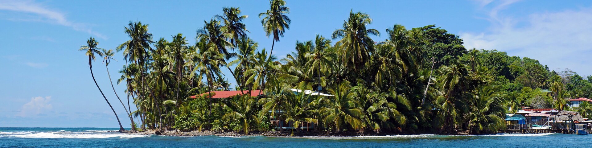 Uma ilha tropical com palmeiras e um edifício com telhado vermelho.