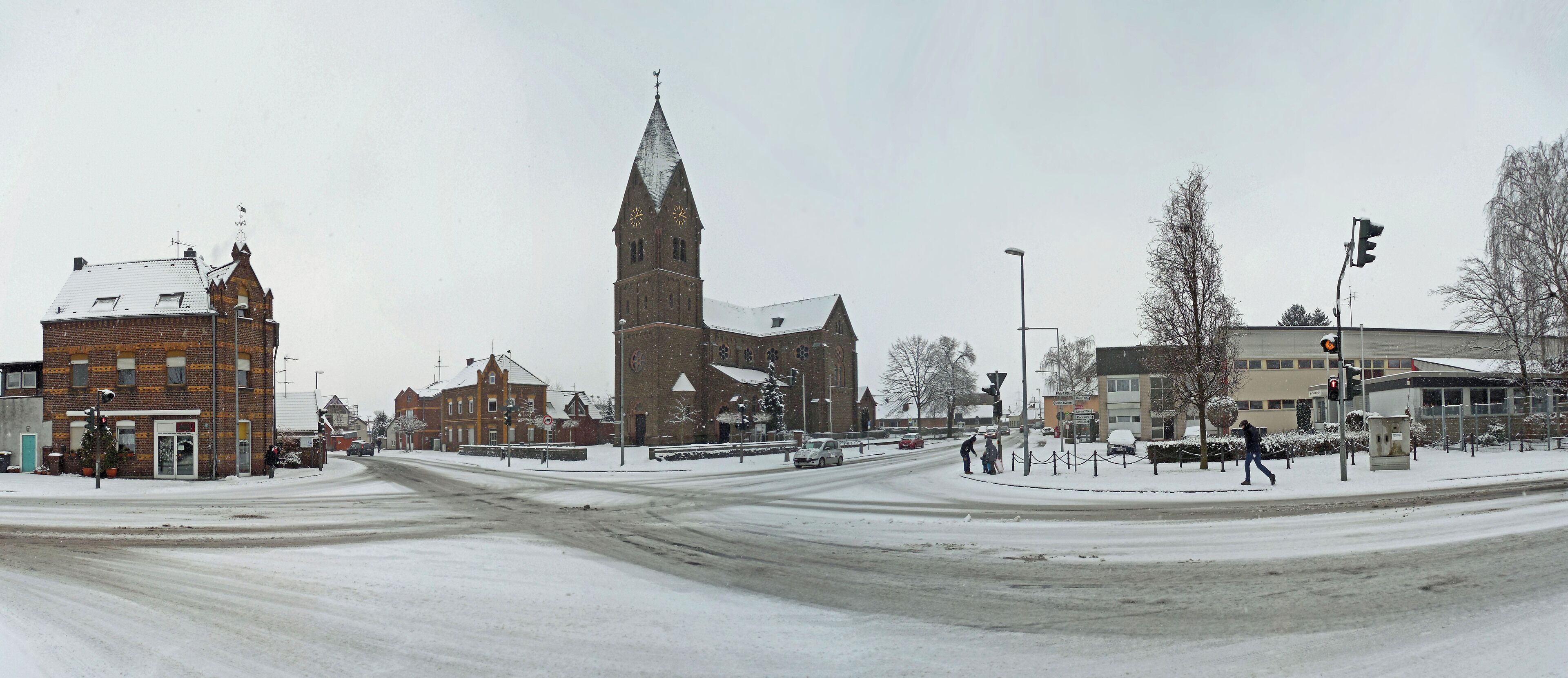 A snowy intersection with a church, a brick building, and a roundabout.