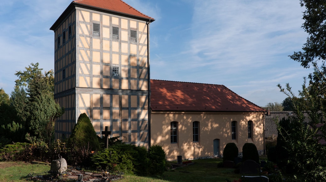 En kirke med et tårn og et rødt tag, omgivet af grønt og træer.