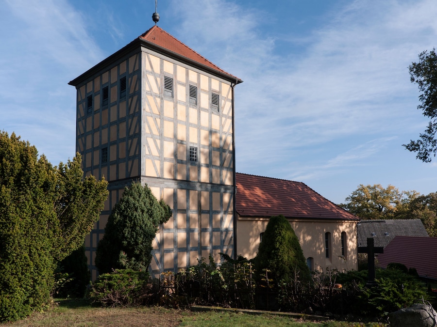 A church with a tower and a red roof, surrounded by trees and a grassy area.