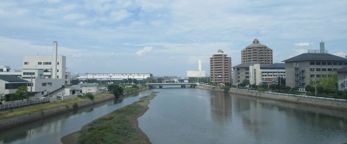 A river meandering through a city with modern buildings and a bridge in the distance.