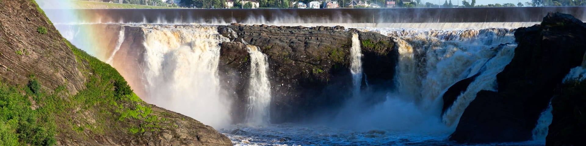 A waterfall with a rainbow, a river, and a rocky landscape.