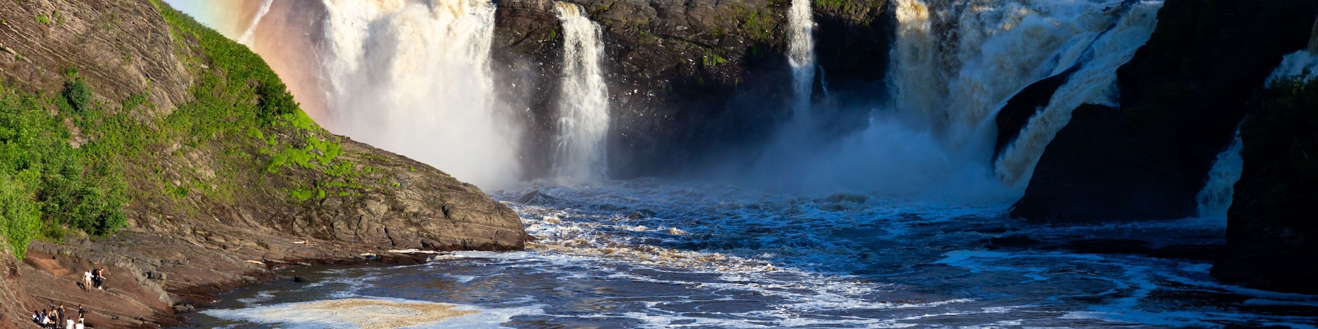 A waterfall with a rainbow, a river, and a rocky landscape.