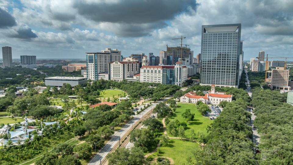A cityscape with a prominent modern skyscraper, historic buildings, and a well-maintained park with a jogging path.