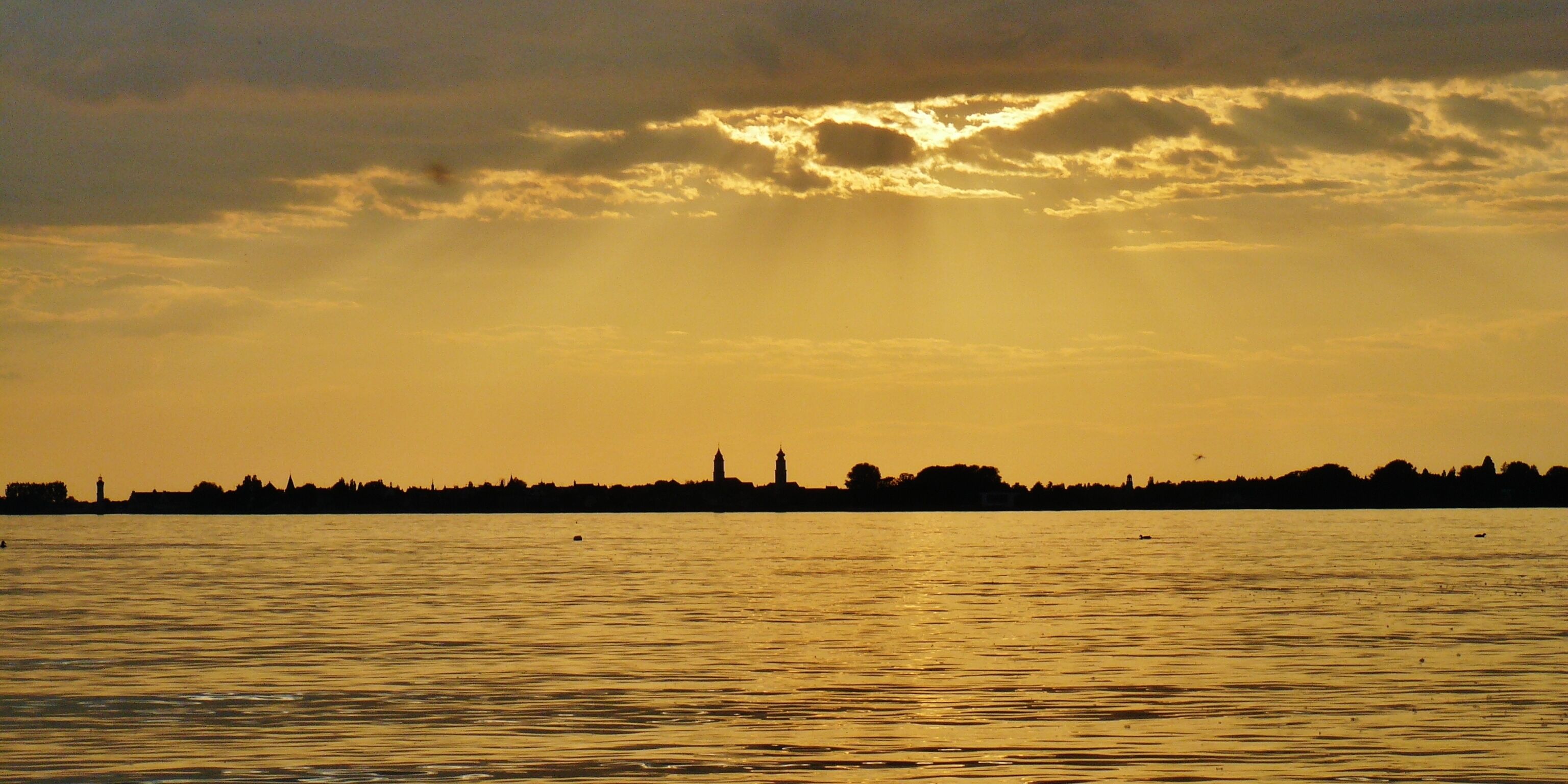 A sunset over a body of water with a silhouette of a city skyline in the background.