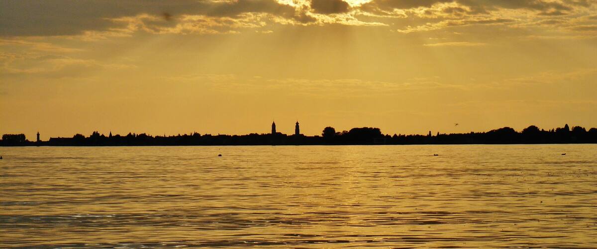 A sunset over a body of water with a silhouette of a city skyline in the background.