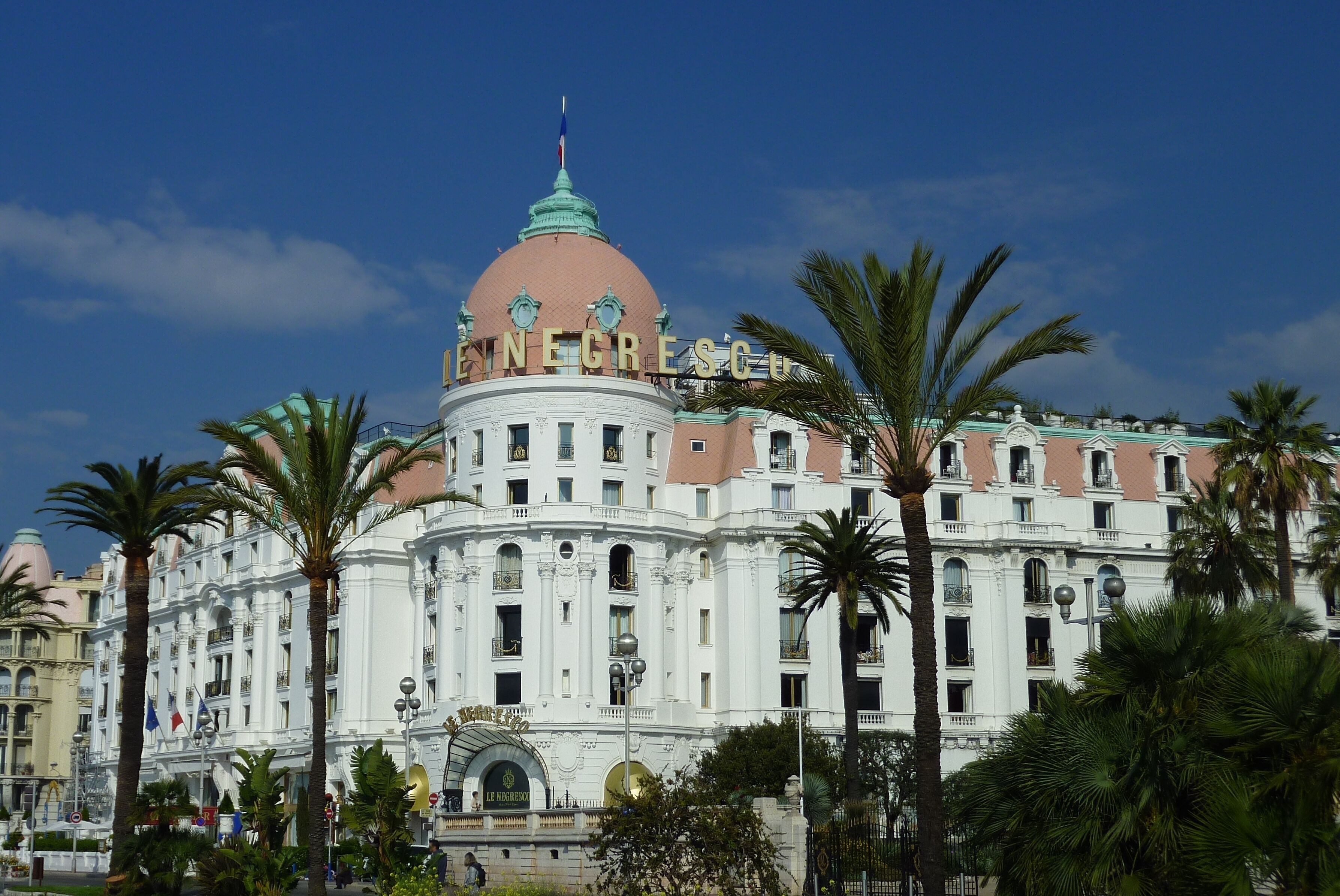 Un edificio grande y ornamentado con una cúpula destacada y varios balcones, rodeado de palmeras.