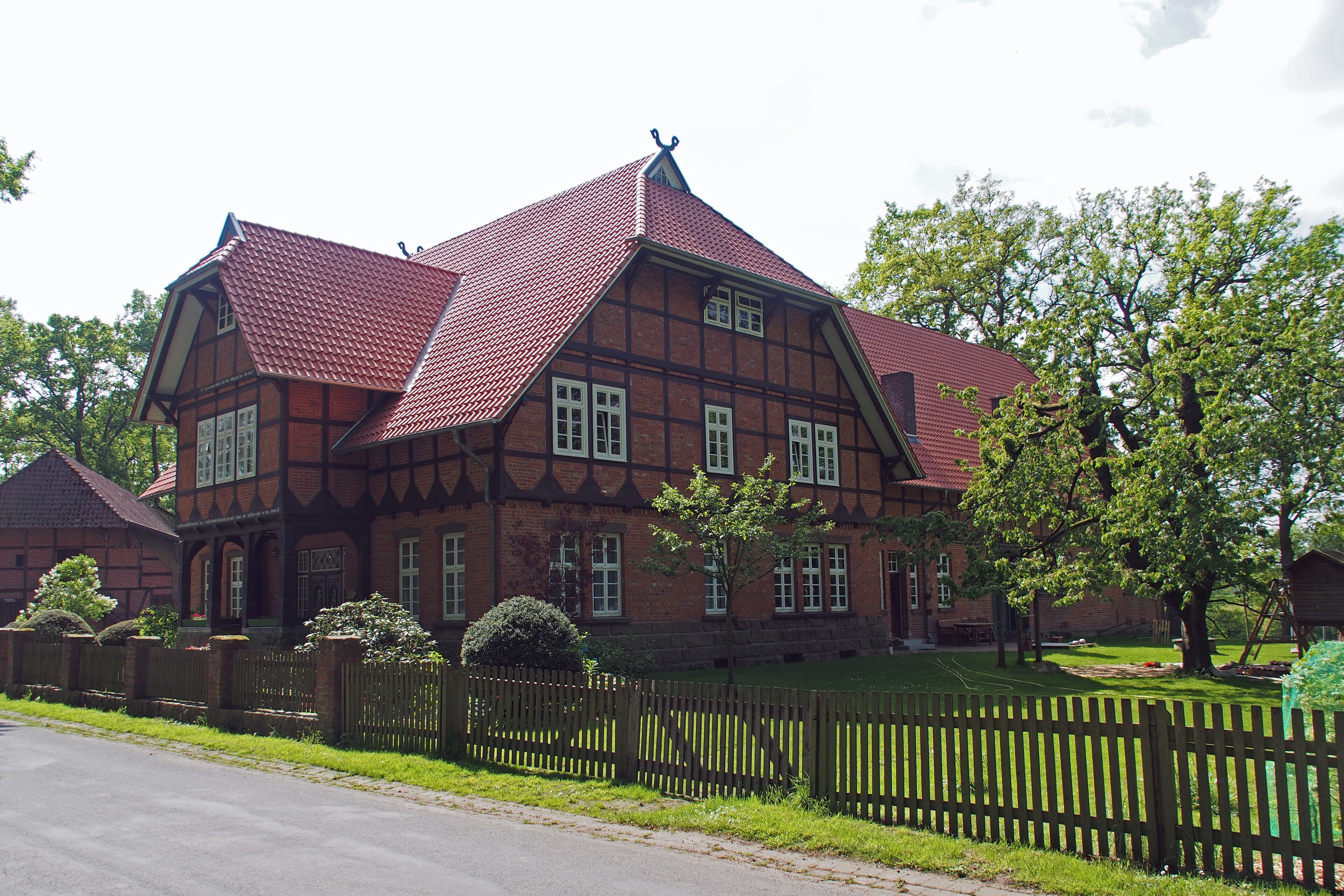 A large, historic half-timbered house with a red-tiled roof and a wooden fence in front.