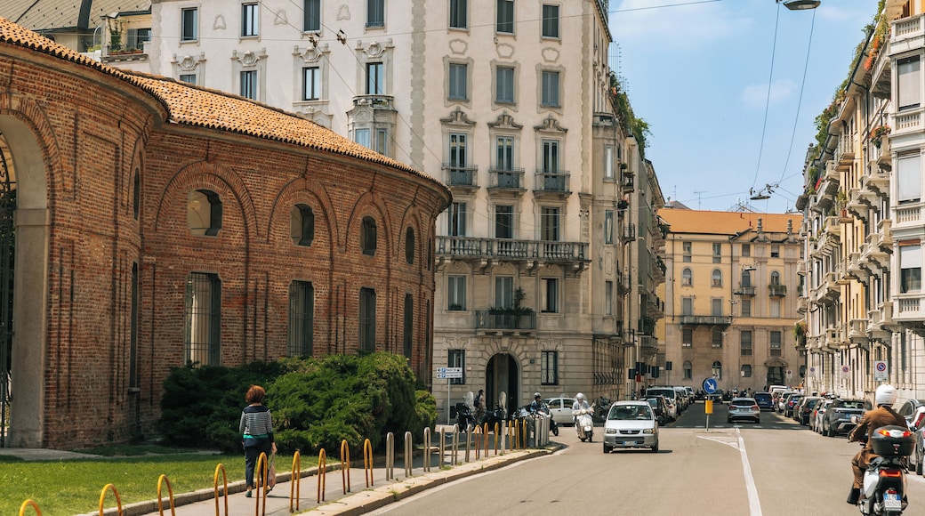 A street lined with historic buildings, a brick structure with arched windows, and a row of parked cars.