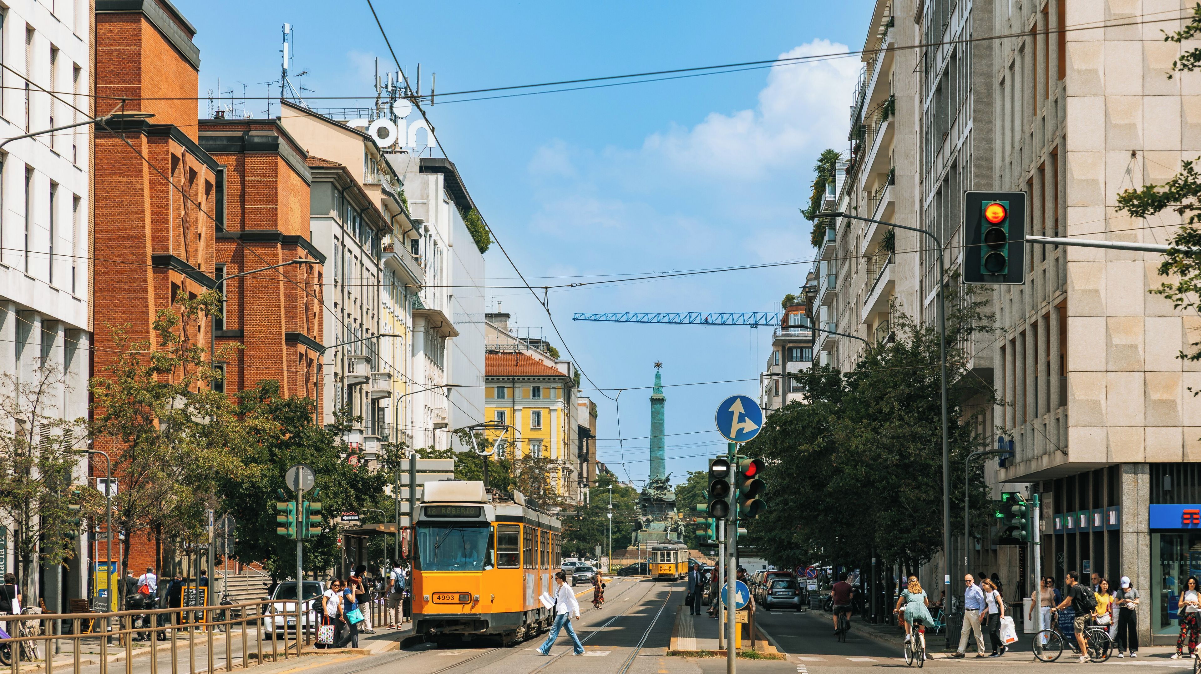 A tram on a city street with buildings and a clear sky.