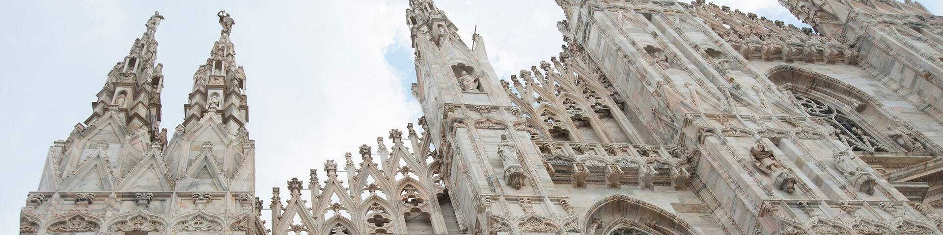 Gothic style with statues of people Duomo di Milano gothic cathedral church, Milan, Italy against blue sky with clouds