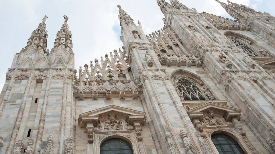 Gothic style with statues of people Duomo di Milano gothic cathedral church, Milan, Italy against blue sky with clouds