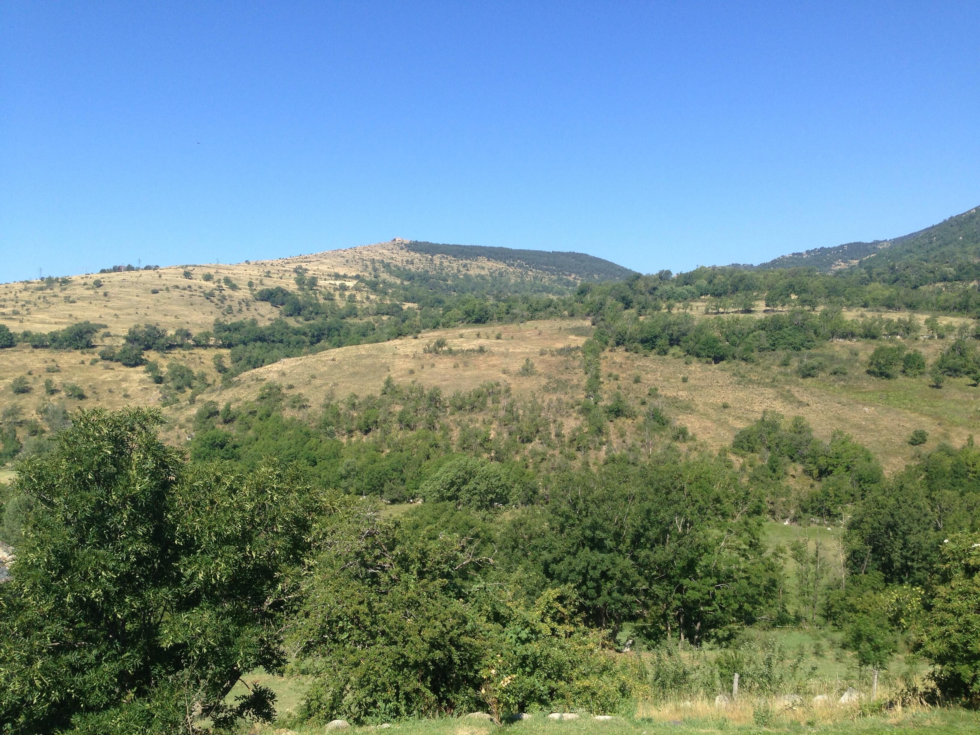 A hilly landscape with dense green vegetation and a clear blue sky.
