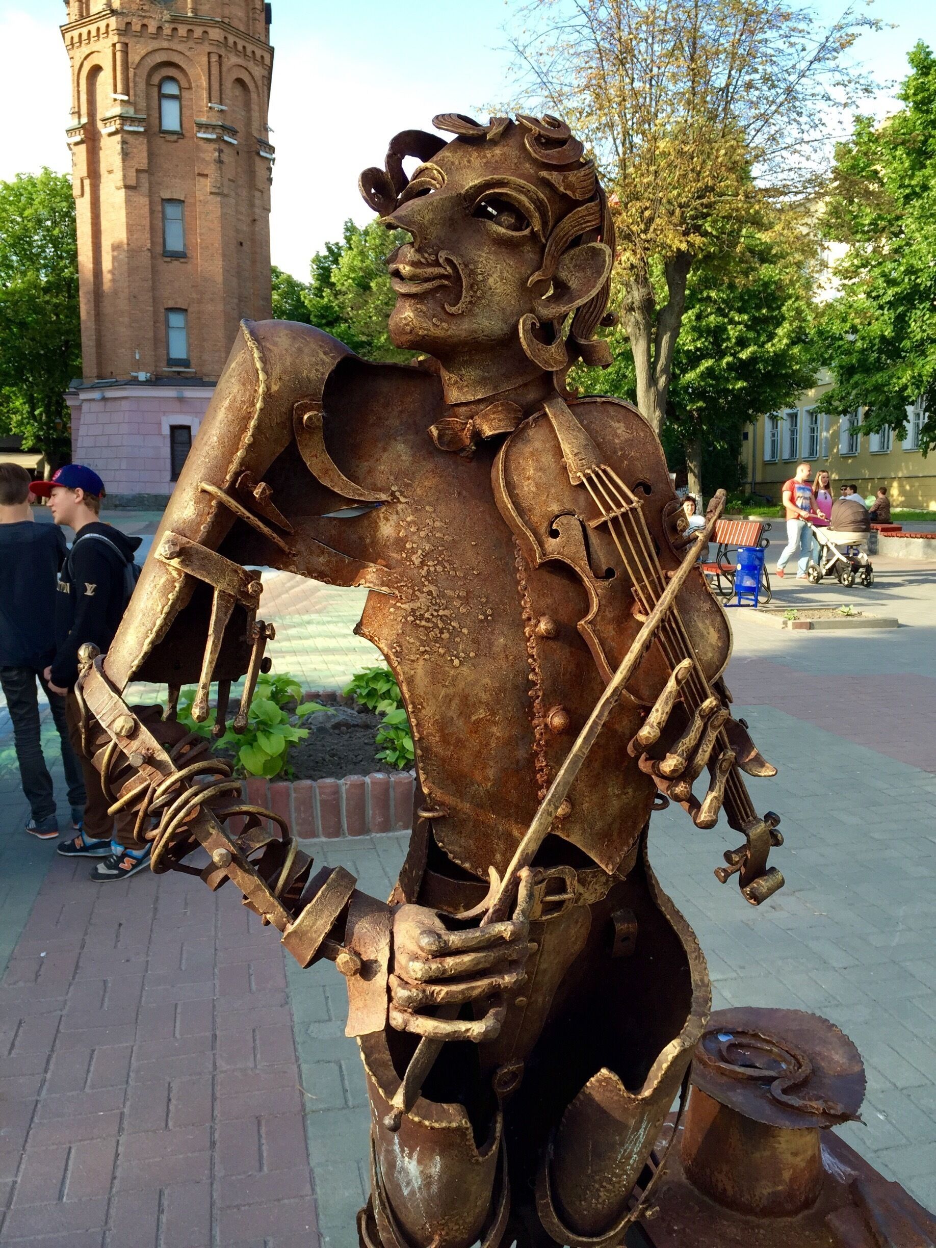 A statue of a violinist made of rusted metal in a public square.