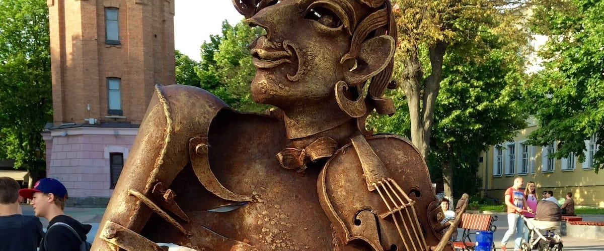 A statue of a violinist made of rusted metal in a public square.