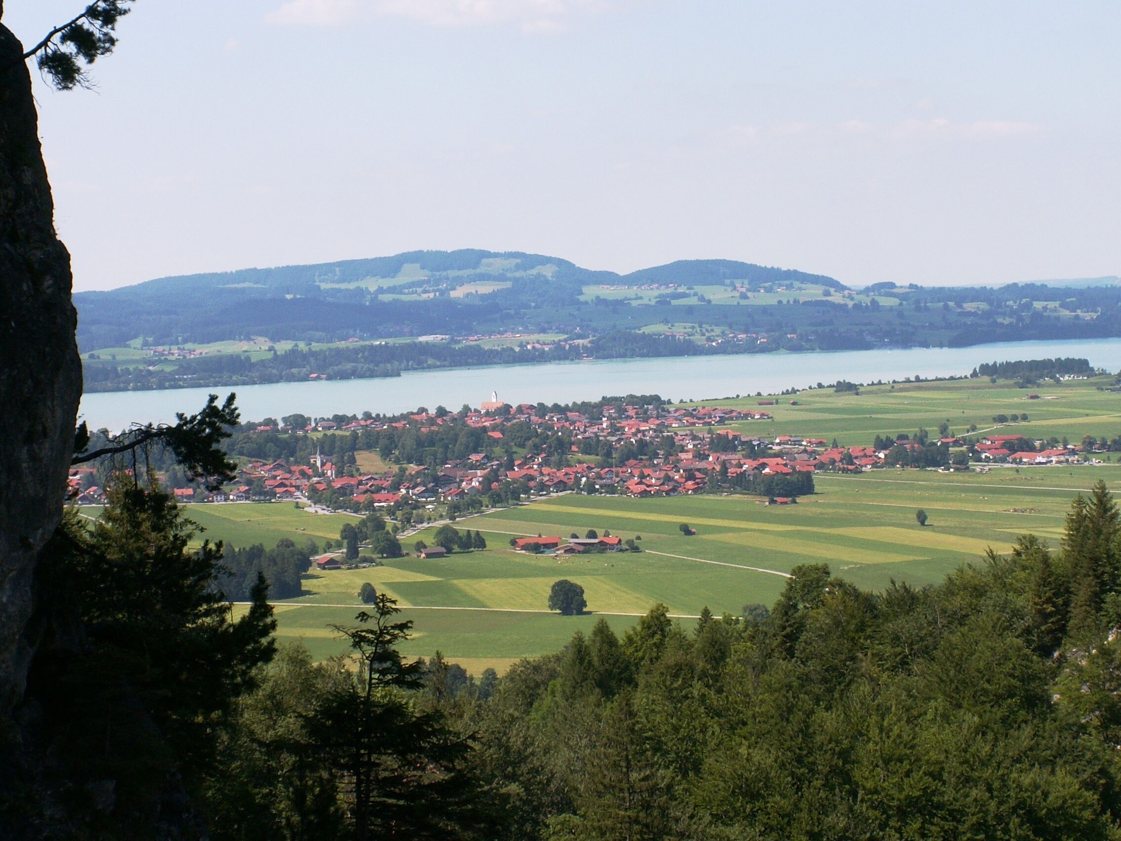 A town with red-roofed houses by a lake, surrounded by green fields and hills.