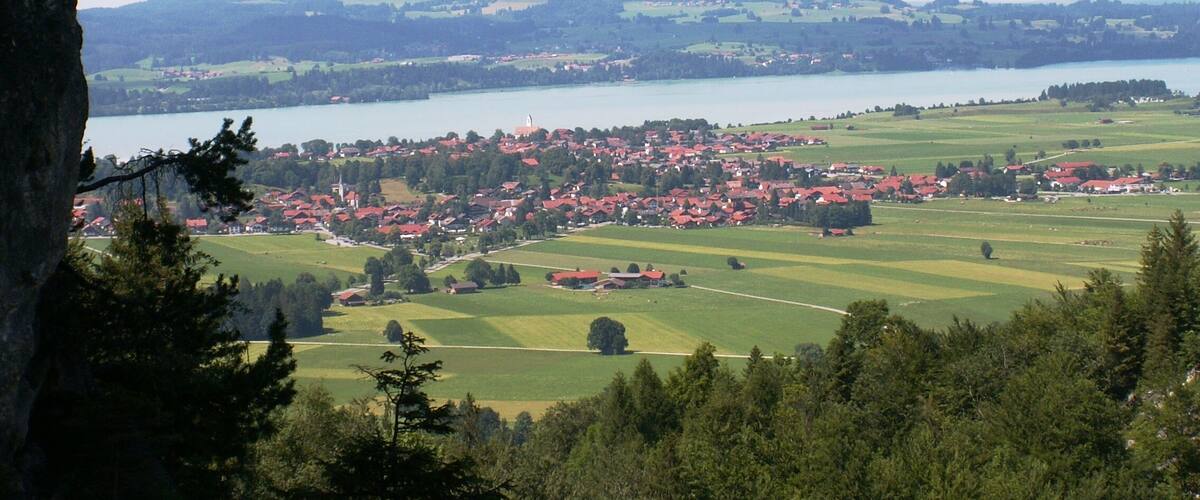 A town with red-roofed houses by a lake, surrounded by green fields and hills.