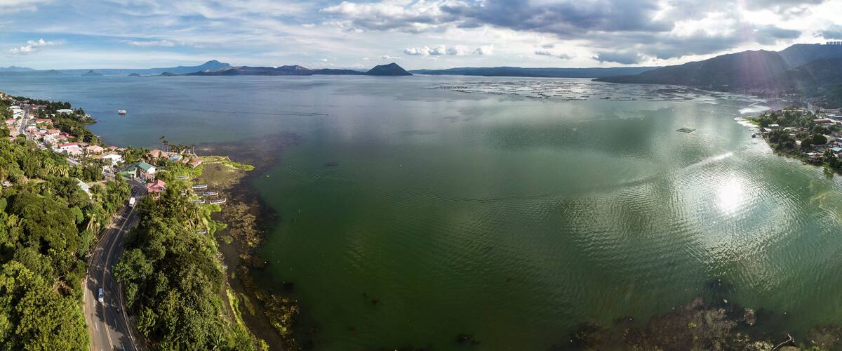 Panorama of Taal volcano and caldera, the coastline of the lake, the town of Laurel, and the Tagaytay mountain ridge.