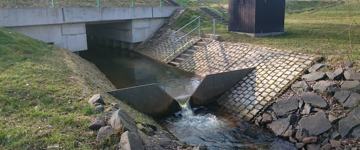 A concrete bridge over a small stream with a wooden structure nearby.