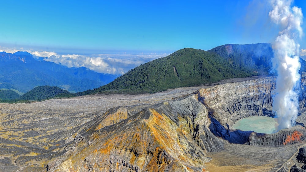Un paysage volcanique caractérisé par un geyser imposant, un terrain accidenté et des montagnes lointaines.