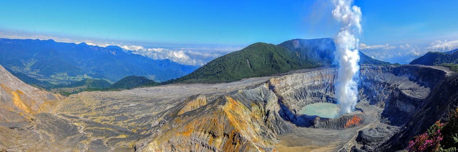 Un paysage volcanique caractérisé par un geyser imposant, un terrain accidenté et des montagnes lointaines.