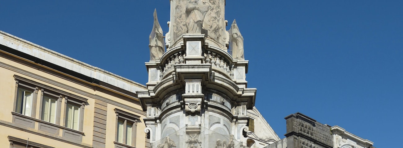 A historic monument with intricate carvings and statues, surrounded by classical architecture and a clear blue sky.