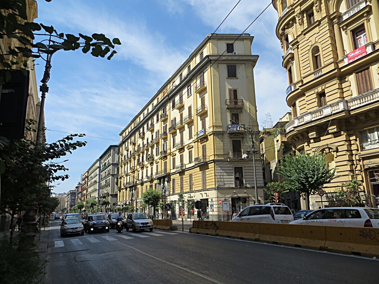 Una calle bordeada de edificios históricos amarillos, un paso de peatones y automóviles estacionados.