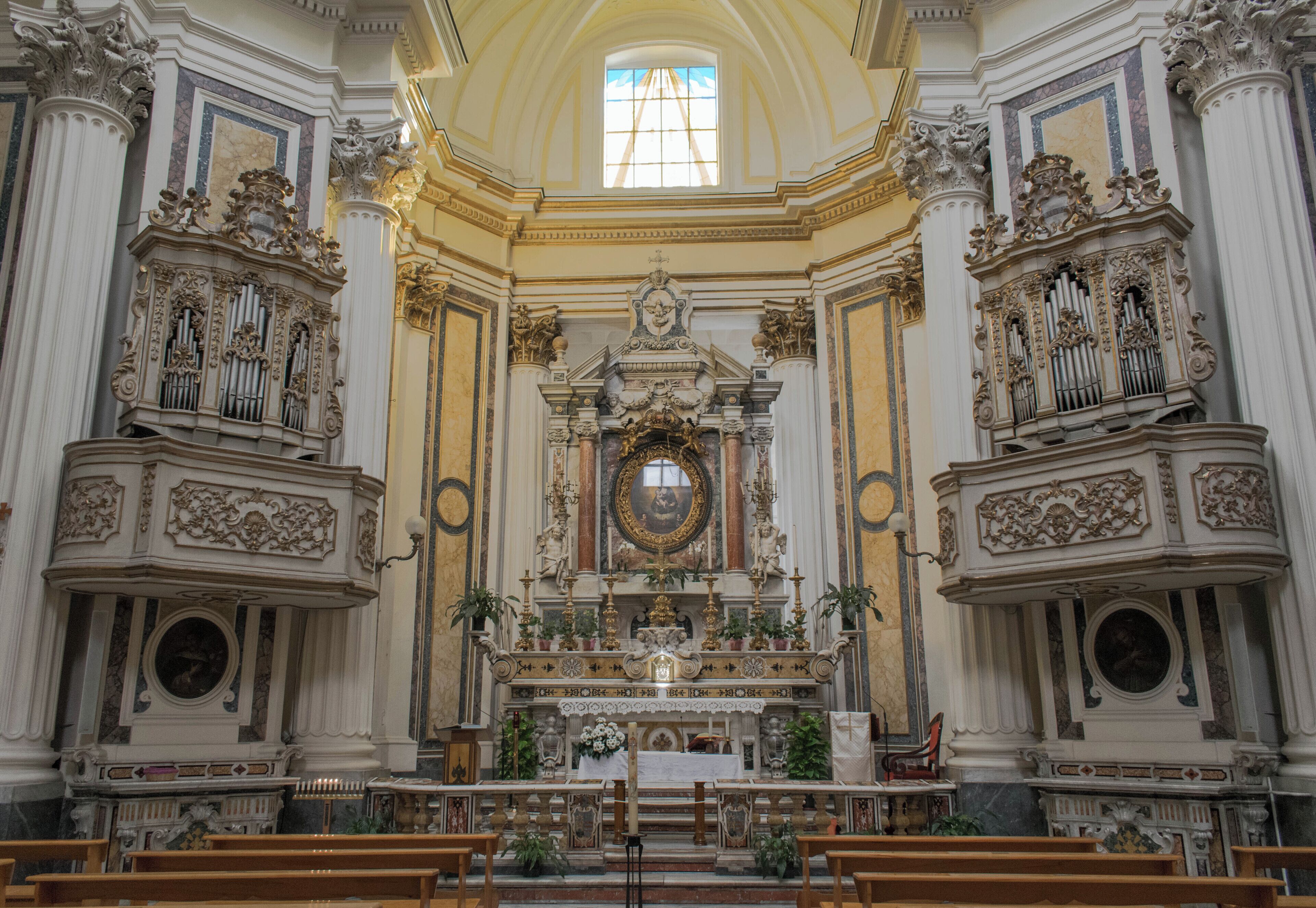 L ’intérieur d’une église richement décorée, avec un autel principal imposant, des colonnes ornées et une grande fenêtre.