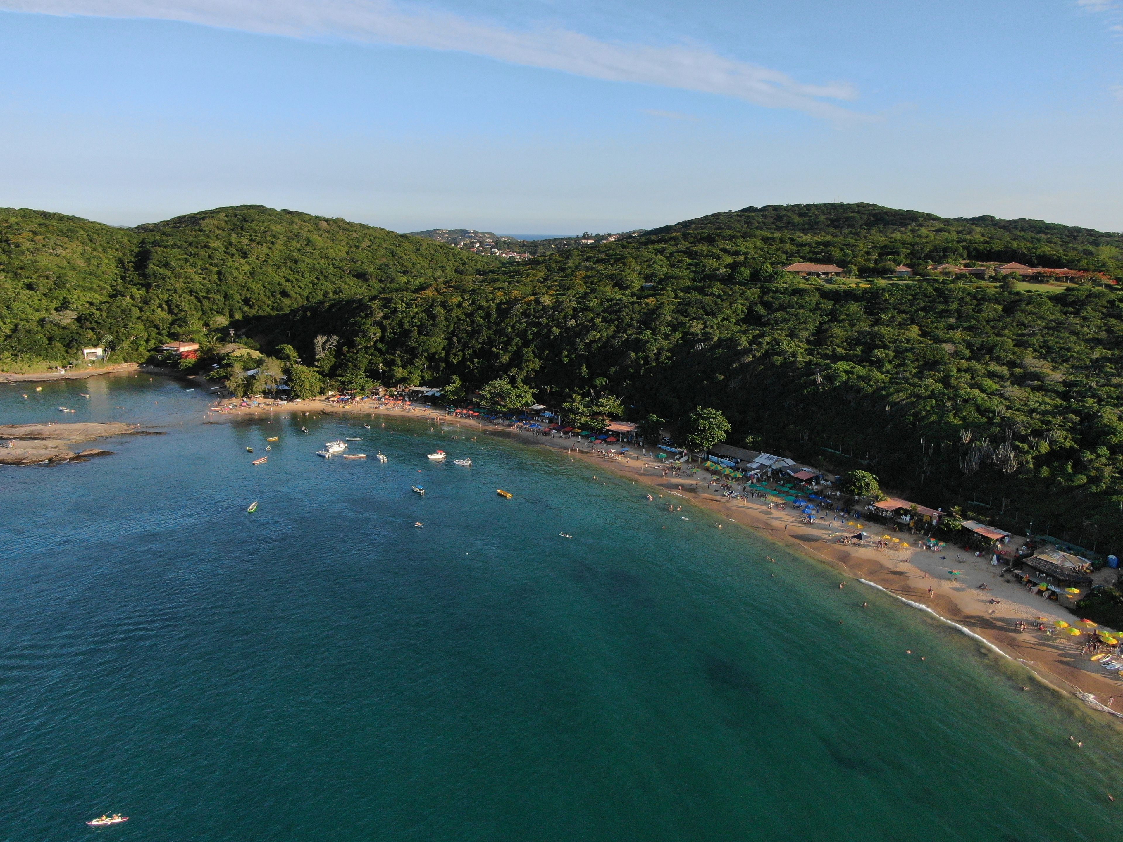A coastal area with a beach, boats, and a forested hillside.