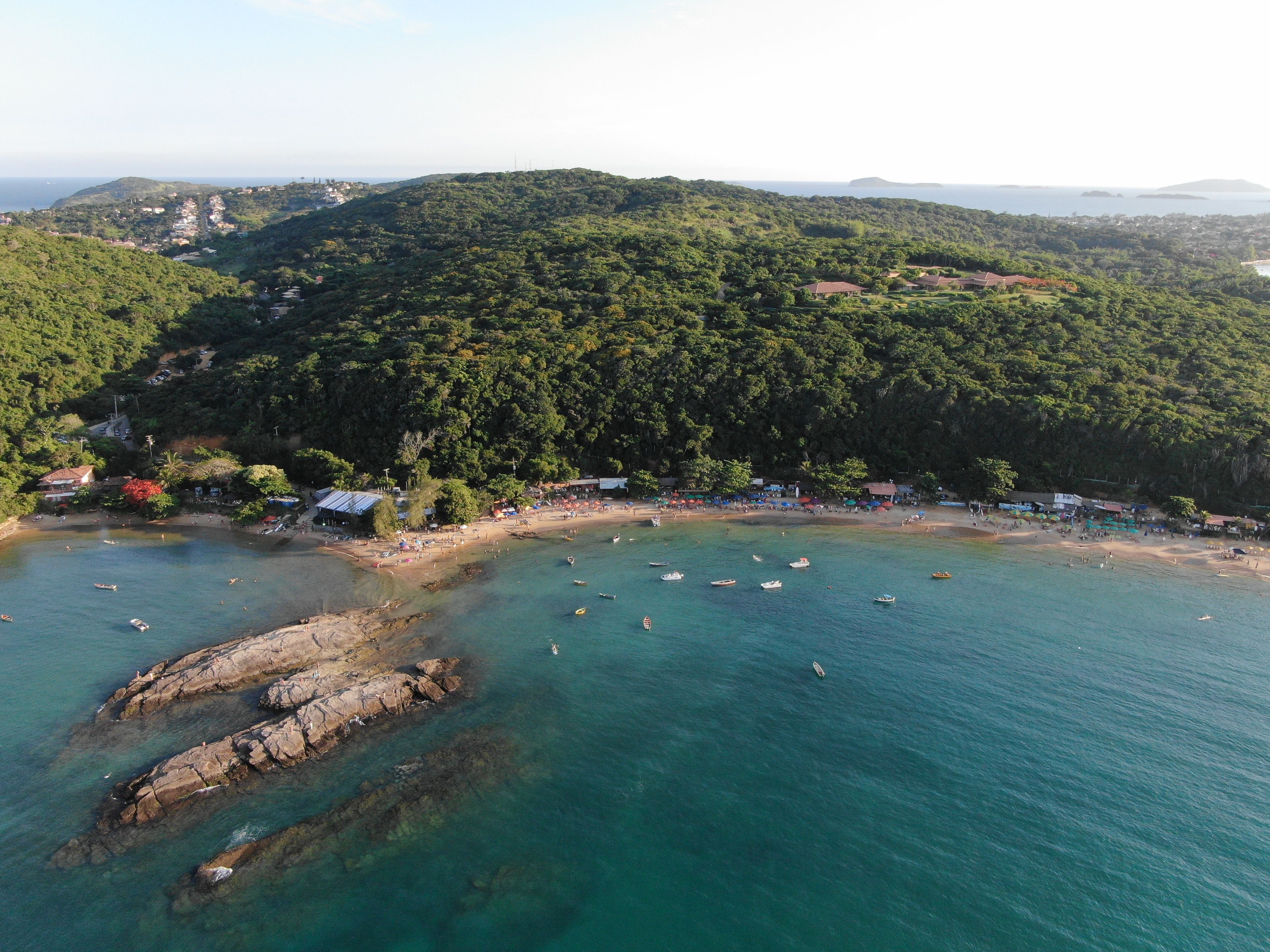 A coastal area with a beach, boats, and a forested hill.