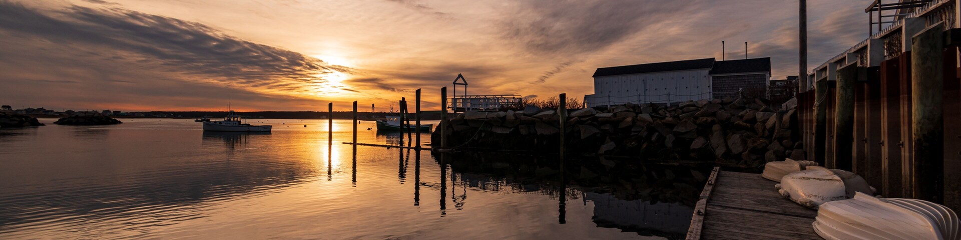 A sunset over a calm harbor with boats, a wooden dock, and a building in the background.