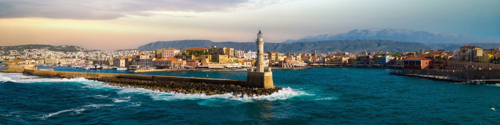 A coastal cityscape with a prominent lighthouse, a harbor with boats, and a mountainous backdrop.