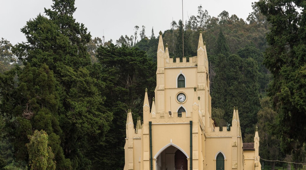 Ooty, India - October 25, 2013: The yellow painted castle-like Saint Stevens Church in Ooty. Red dirt and rose garden with dark green foliage in background.
