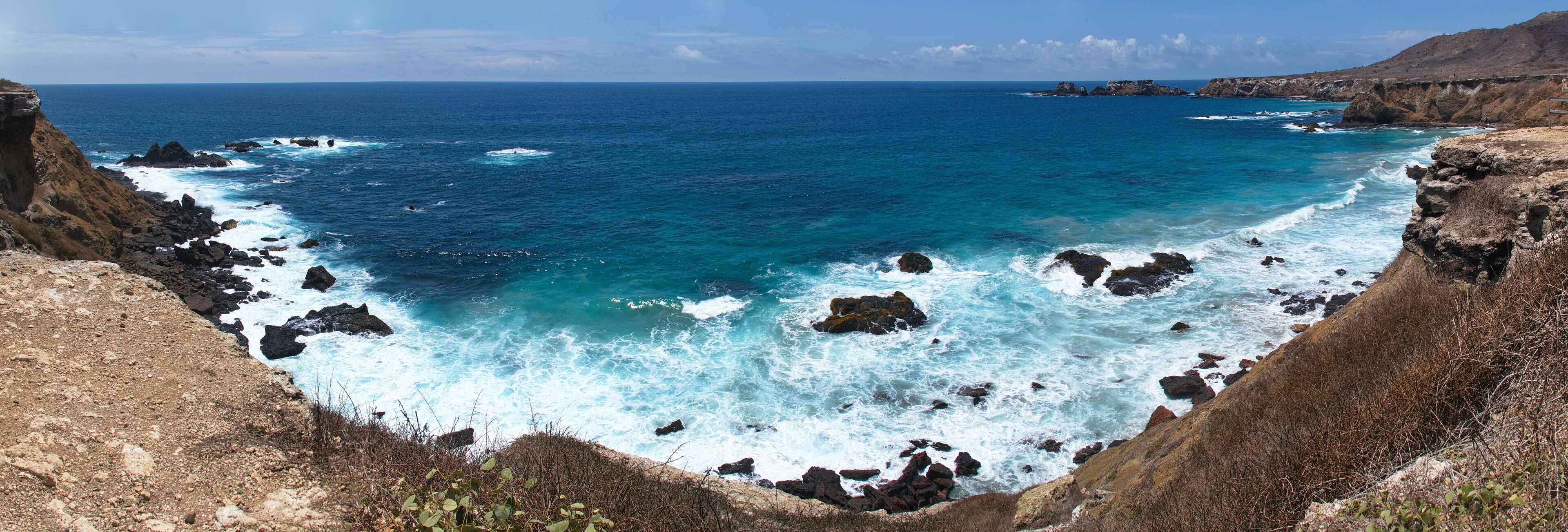 A rugged coastline with rocky cliffs and turbulent sea waves crashing against the rocks.