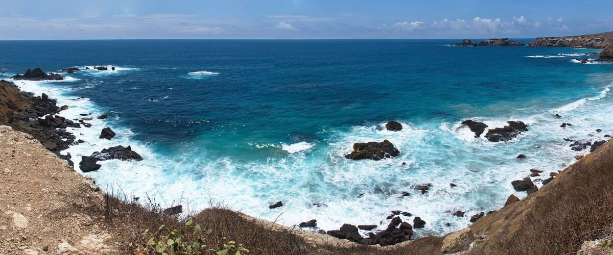 A rugged coastline with rocky cliffs and turbulent sea waves crashing against the rocks.